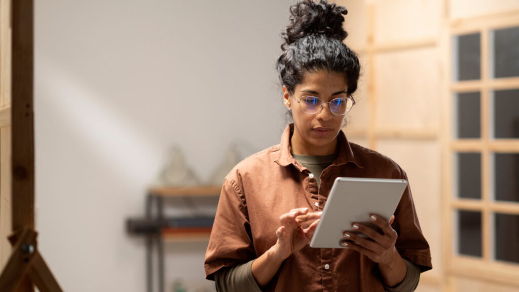 A focused woman with glasses and a high bun using a Artificial Intelligence in a workshop environment, surrounded by soft lighting and wooden elements.